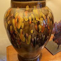 Close-up of ceramic lamp body showing milk chocolate brown background with tangerine, lemon yellow, white, and black brushstroke splotches and glossy finish.