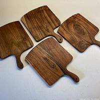 Four matching small wooden charcuterie boards laid out on white surface showing wood grain and handle details