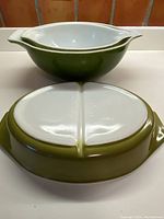 View showing the bottom side of the divided casserole dish and one mixing bowl stacked inside the larger bowl, highlighting the avocado green exterior and white interior separation.