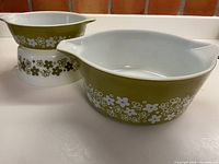 Three vintage Pyrex casseroles in avocado green with white Crazy Daisy floral pattern, showing exterior side views and pattern details