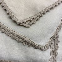 Close-up of hand crocheted scalloped edging on linen napkins showing intricate crochet loops and fine linen weave.