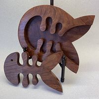 Wooden fish-shaped hot plate with removable fishbone-shaped puzzle piece on display stand.
