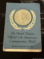 Medal secured in blue card holder with white United Nations olive wreath design and text indicating it is an official 25th anniversary commemorative medal in solid sterling silver