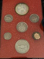 Set of seven Canadian coins displayed in red fabric-lined case including a large double dollar coin with mounted figure and smaller denominations