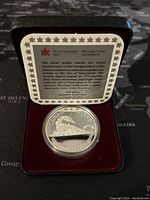 Silver proof dollar coin displayed in red velvet case with a card from Royal Canadian Mint describing the 100th anniversary of the transcontinental railroad and Vancouver.