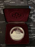 Canadian silver proof dollar coin in protective capsule, displayed inside a burgundy velvet lined case with maple leaf emblem.