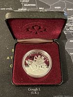 Silver proof dollar coin in maroon velvet display case with maple leaf motif on inner lid.