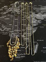 Four sterling silver necklaces laid out on a world map background. One necklace has a decorative fringe made of small leaf-shaped links, the other three have various chain designs. All appear shiny and in good condition.