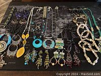 Full overview of various colorful jewelry pieces spread on dark surface, including earrings, necklaces, and bracelets arranged in rows