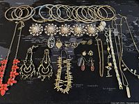Full view of assorted gold-tone bracelets, earrings, and necklaces laid out on a black map background.