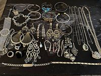 Full view of assorted silver-tone jewelry items including bracelets, earrings, rings, and necklaces laid out on a dark map background.