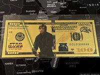 Front of $100 novelty bill featuring Luke Skywalker in gold foil with Star Wars logo and denomination details.
