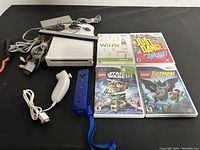 Full lot showing Nintendo Wii console, sensor bar, power and AV cables, white Nunchuk, blue Wii Remote with strap, and four Wii game cases.
