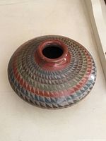 Top angled view of round Navajo ceramic vase with geometric paint pattern in red, blue and earth tones.