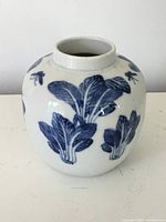 Front view of an antique Chinese ceramic ginger jar displaying blue painted leafy vegetable and insect motifs on white glazed surface.