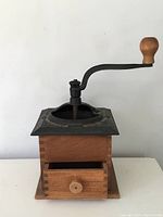 Front view of antique farmhouse coffee grinder showing cast iron top with crank handle and open wooden drawer in base.