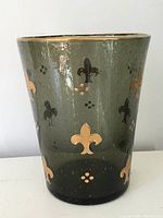 Full view of green antique glass vase with applied gold fleur-de-lis details on its surface and gold rim on top.