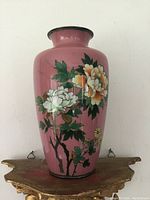 Front angle showing pink cloisonne body with white and orange floral decoration against green leaves.