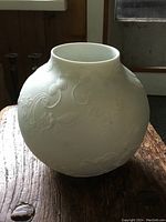 White porcelain spherical vase showing side embossed floral and peacock details on wooden surface