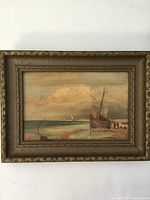 Full front view of the oil painting in its antique frame, showing boats on a shore under cloudy sky with surface wear and signature.