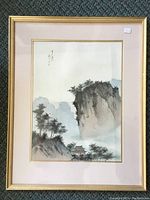 Full view of the framed Chinese print showing landscape with mountains, trees and a small building, surrounded by double mat and gold-tone frame.
