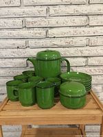 Full tea set displayed on wooden slatted surface with green glaze and dark rim accents visible. Includes teapot, creamer, sugar bowl, six cups, and six saucers.