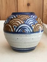 Front view of vase showing blue and brown repeating wave pattern on upper half with light beige salt glazed base.