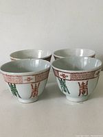 Front view of four antique Chinese porcelain tea cups showing hand painted red geometric and green Chinese characters design