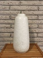 Front view of the tall white textured ceramic vase with a cylindrical body and subtle tapering, placed on a wooden surface.