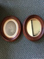 Two oval antique mahogany frames side by side on carpet, one frame fitted with an antique photo and the other with a mirror.