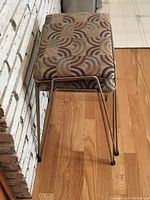 Side angle showing fabric seat with geometric pattern, chrome tubular legs and rubber feet (one visible) on stool.