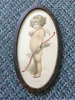 Front view of oval framed print showing cupid holding bow and arrows, artist signature and caption visible