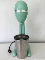 Front view of vintage Hamilton Beach milkshake maker showing mint green motor body and stainless steel mixing cup in place.