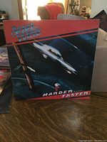 Front cover of April Wine Harder... Faster album, showing graphic of speeding car and red-black design.