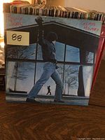 Front cover of Billy Joel Glass Houses LP showing broken window with reflection of man in jacket and jeans.
