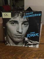 Front cover of The River featuring Bruce Springsteen black-and-white close-up portrait with blue text.