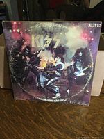 Front cover of Kiss 'Alive' album showing the band performing on stage with colorful lighting and smoke.