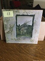 Front cover of Led Zeppelin IV vintage LP showing man carrying bundle of sticks artwork with worn, discolored, and peeling cover.