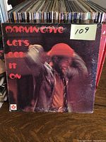 Front cover of Marvin Gaye's "Let's Get It On" vinyl LP showing album art with artist in red hat, red text, and condition wear from use.