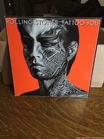 Front cover of Tattoo You LP showing black and white tattooed face on orange background