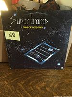 Front cover of Supertramp Crime of the Century vinyl LP. Shows album artwork with hands behind bars in space theme. Sticker with '68' number on front.