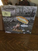 Front cover of Supertramp Crisis? What Crisis? vinyl LP showing industrial background with beach scene foreground.