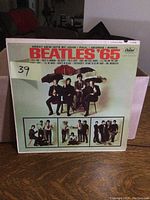 Front cover of Beatles '65 album featuring The Beatles sitting under umbrellas and track titles at top