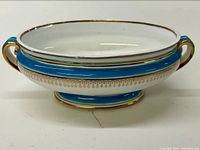 Oval turquoise and gilt decorated porcelain tureen with two handles and visible hairline crack on base.