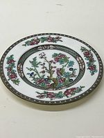 Top-down photo of the round plate showing the full floral and patterned design with predominant colors pink, green, blue, and brown on white ceramic.