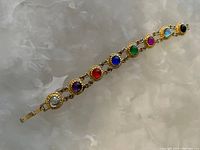 Photo of a gold-tone bracelet with eight colorful round stones on a white crystal background