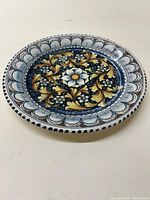 Full view of vintage round ceramic plate with blue, gold, white floral and scroll design.