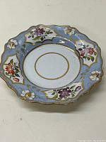 Full view of the antique decorative plate showing floral hand painted designs and scalloped edges with gold accents.