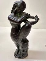Front side angle view of the bronze figurine showing the seated female musician playing a mandoline, surface patina visible.