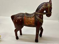 Front side view of the brown wooden horse figurine with hand-painted floral and gold detailing, showing saddle and carved features.
